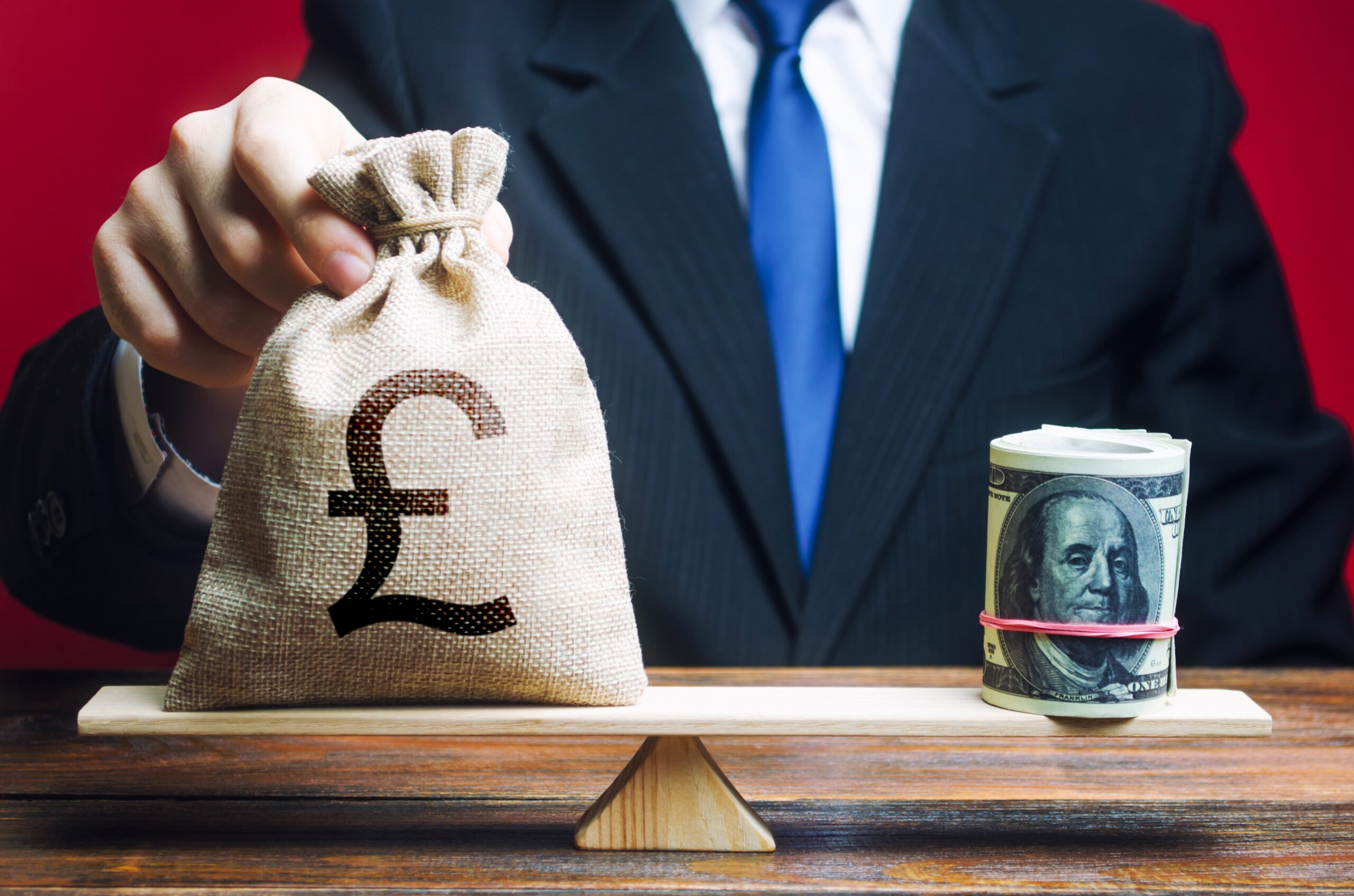 A man puts a pound sterling GBP money bag on the scales opposite to the dollar. Exchange rate, comparison of economic indicators. Investments in foreign currency bonds. Avoiding savings inflation.